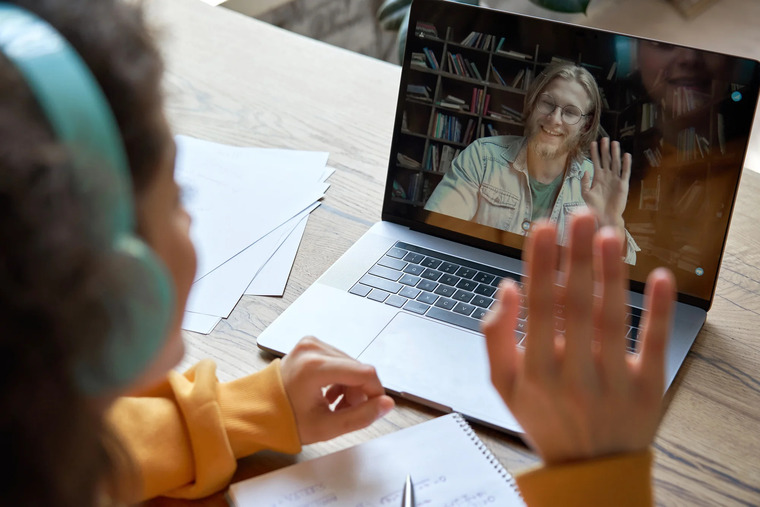 A child seated at a desk, hands raised, indicating participation or excitement in a meeting or discussion.