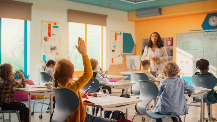 elementary school classroom with students raising their hands and a teacher standing at the front, engaging the class during a lesson