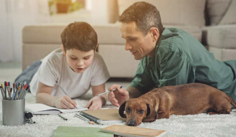A man and a boy are writing on a white rug, while a dog sits nearby, creating a cozy indoor scene.