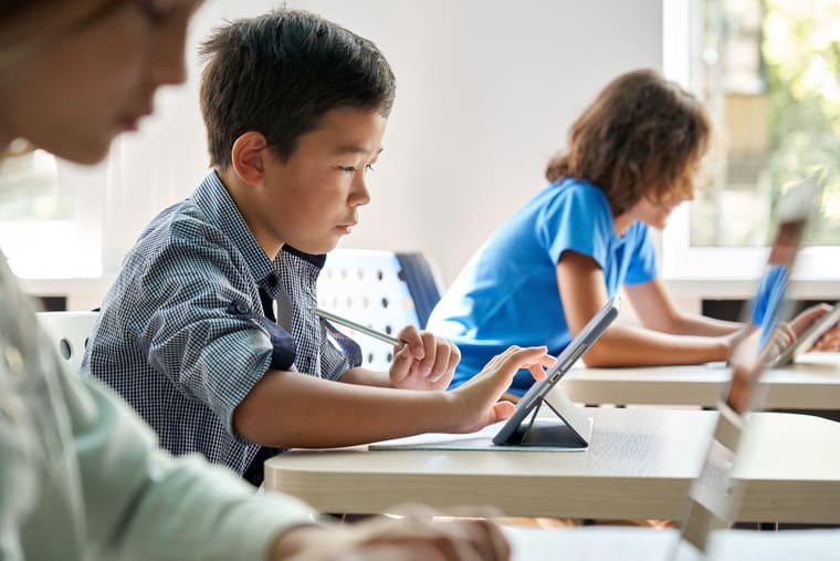 A boy and girl sit at desks, focused on their laptops, engaged in a study session together.