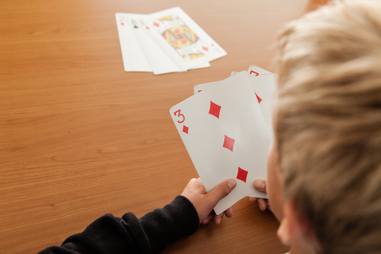 Child holding oversized playing cards, perfect for hands-on math games that boost number sense