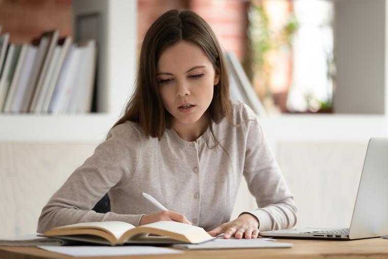 Focused teenage girl studying math at home with books and a laptop, demonstrating independent learning and academic responsibility