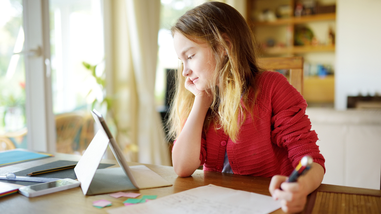Smart preteen schoolgirl doing her math homework with digital tablet at home.