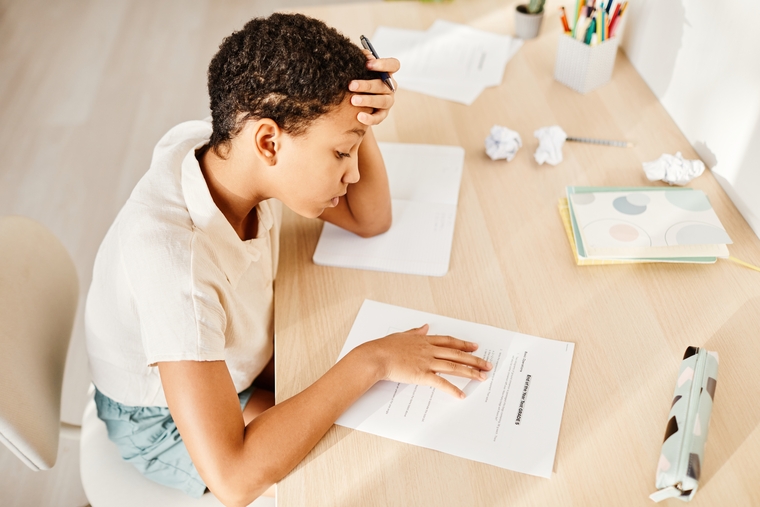 Student sitting at a desk holding their head while reading a worksheet, appearing focused and concerned