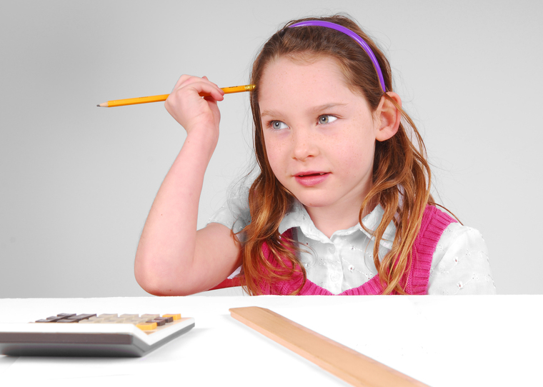 A young girl sitting at a desk, focused on her work with a pencil in one hand and a calculator in front of her.