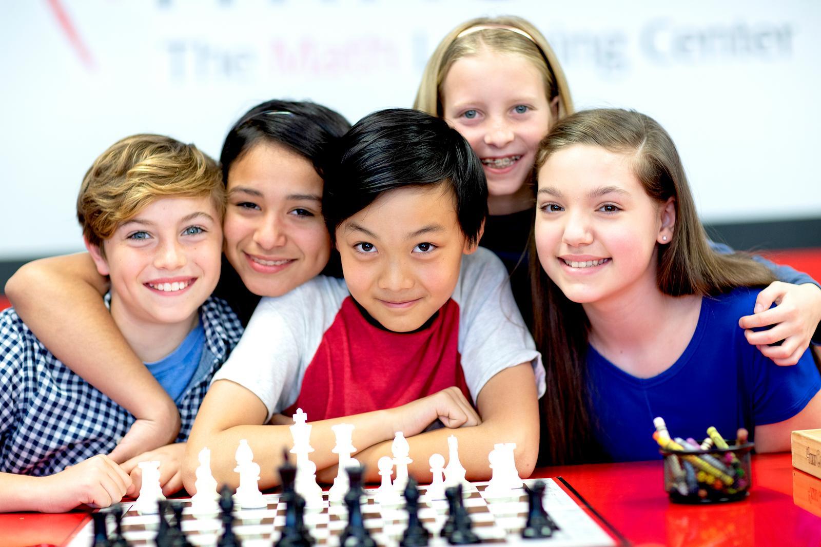 A group of children smile next to a chess board at a Mathnasium Learning Center.