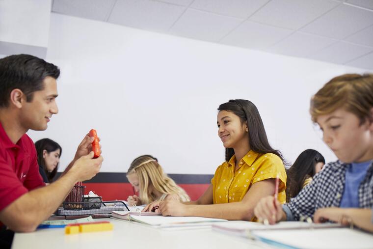 A male tutor assists a group of children at a table during a math session.