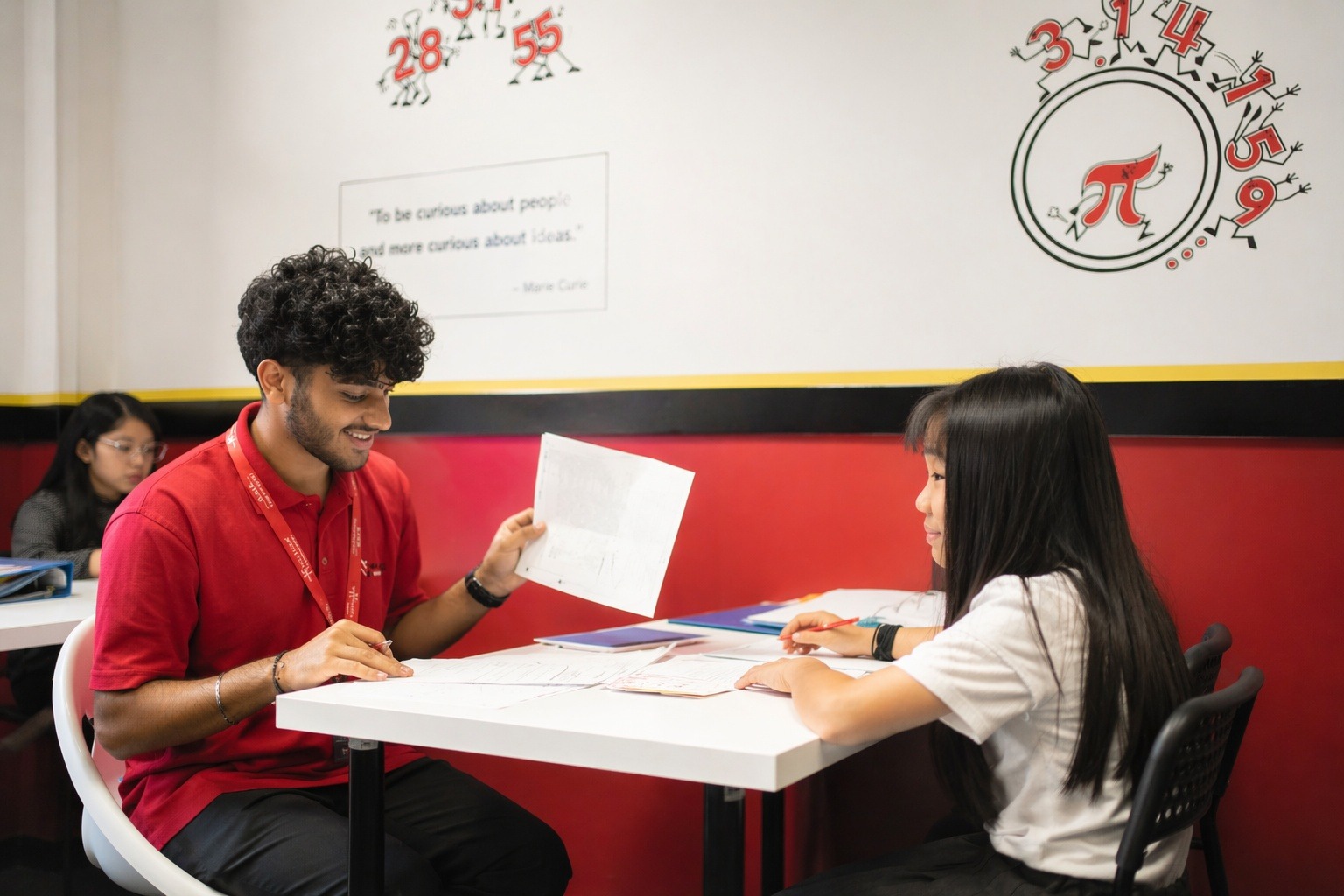A man tutors a girl in math at a table, both focused on the papers in front of them.
