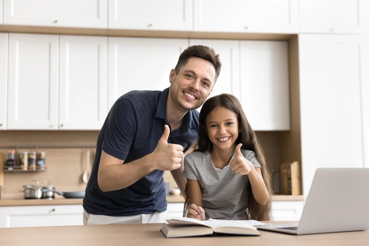 A man and a young girl give thumbs up while collaborating on a laptop, showcasing a positive learning experience.