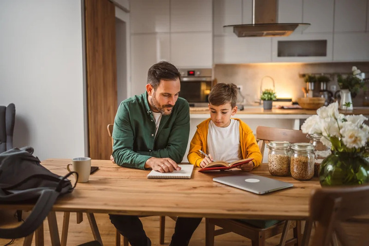 A father and son are seated at a desk, immersed in their books, creating a nurturing learning atmosphere at home.