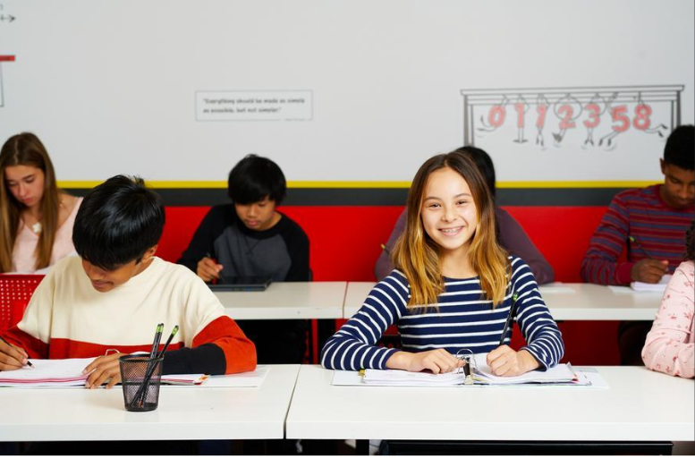 A group of children attentively sitting at desks in a bright classroom, engaged in learning activities.