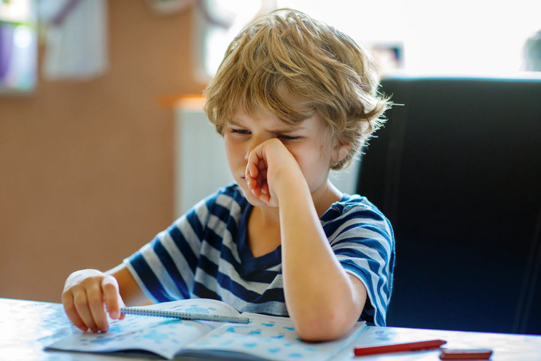 A young boy sits at a table, his hand on his face, expressing reluctance rather than inability to tackle math.