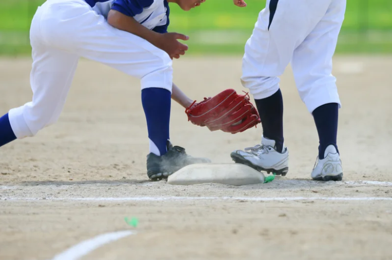 Two boys playing baseball in a grassy field, one batting while the other prepares to catch the ball.
