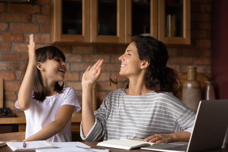 Smiling mother and daughter sharing a high five at the kitchen table after working on math homework together