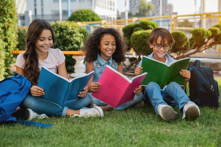 Middle school students sitting on grass reading notebooks