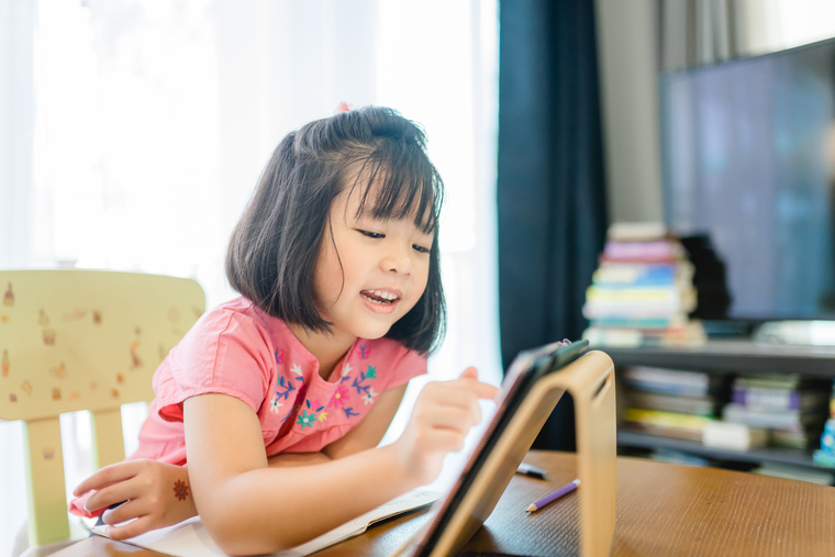 Young girl smiling and learning on a tablet, illustrating the benefits of starting math enrichment early in a child’s education