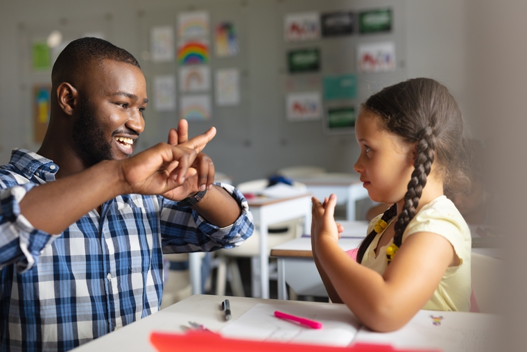 Smiling math teacher teaching sign language to elementary girl.