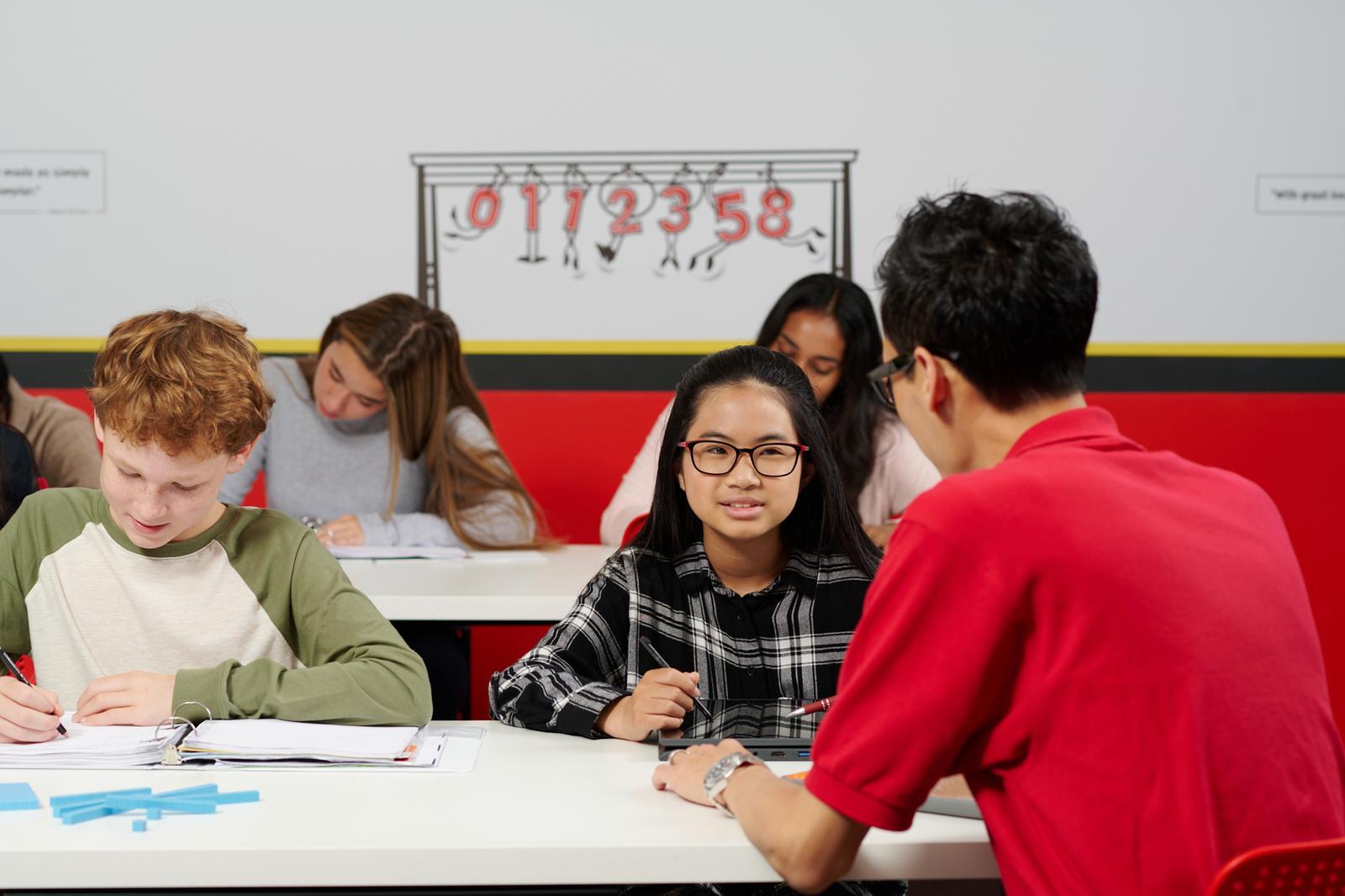 A classroom scene featuring students seated at a table, actively participating in a group project with notebooks and devices.