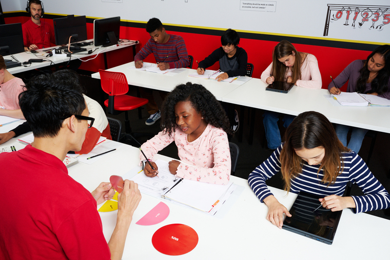 A group of children attentively sitting at desks in a bright classroom, engaged in learning activities.