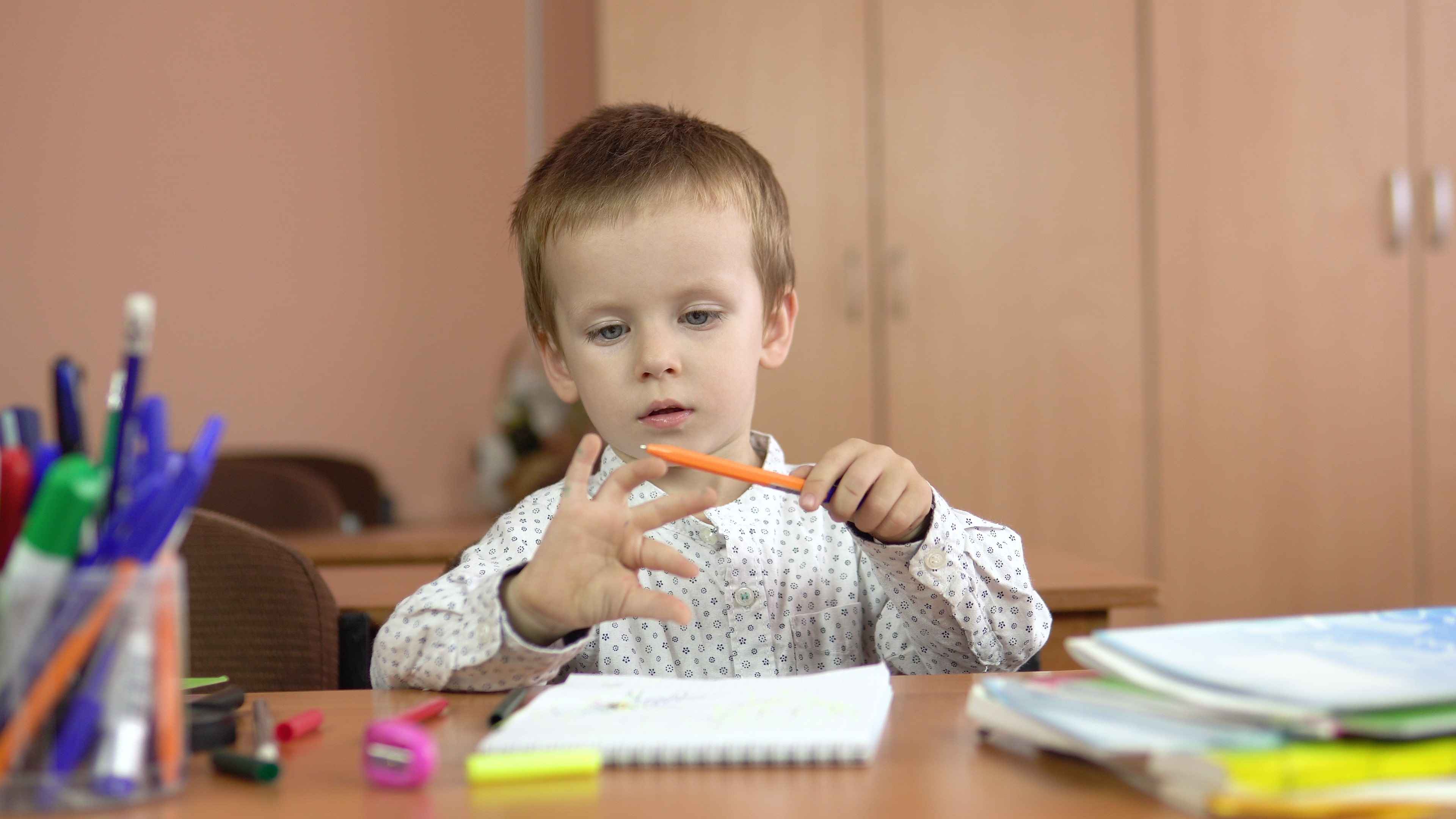 A young boy using a pencil to help him count with his fingers while sitting at a table 