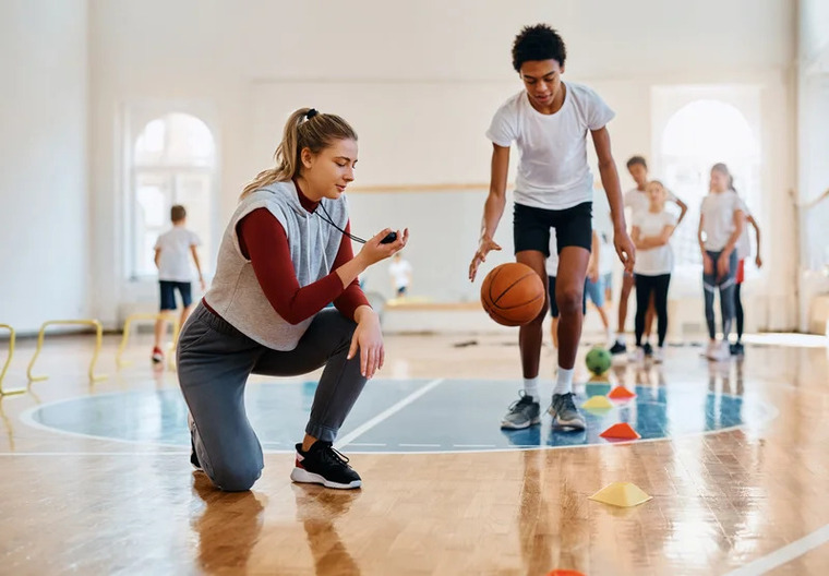 A woman in athletic attire kneels on the court, gripping a basketball, preparing for her next move.