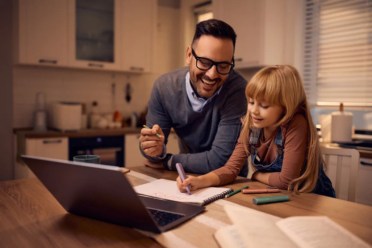A man assists a young girl as they work together on a laptop, both engaged in the activity.