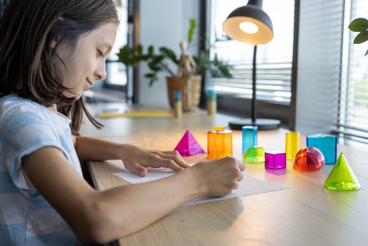 A girl sits at a table, focused on writing with a pencil on a sheet of paper.