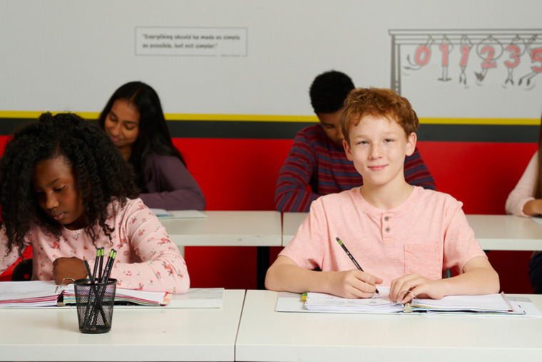 A group of children attentively sitting at desks in a bright classroom, engaged in learning activities.