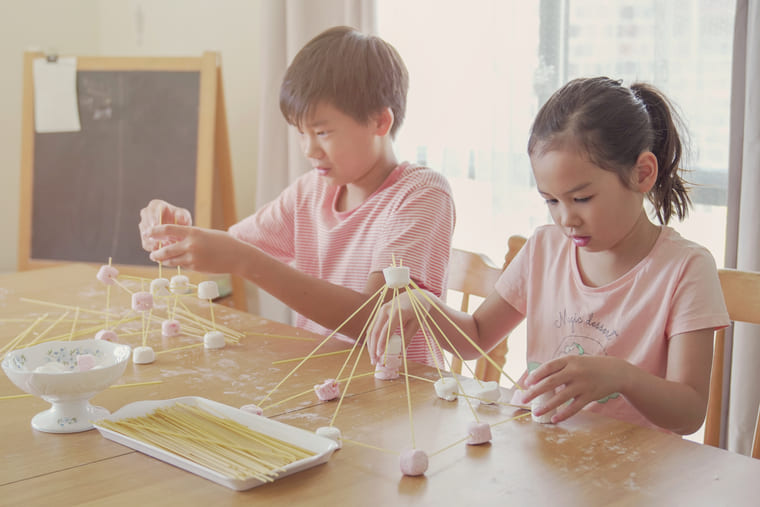 Two children joyfully playing with spaghetti at a table, creating a playful and messy scene.