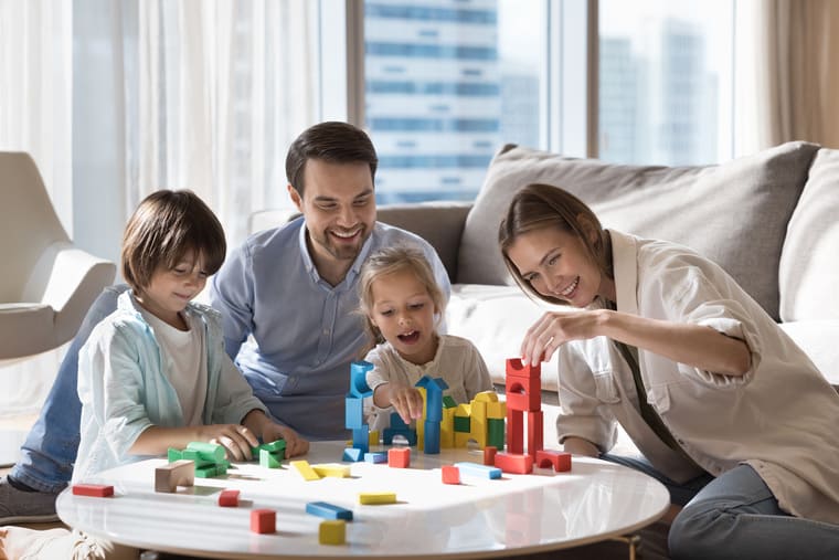 A family joyfully playing with colorful wooden blocks in a cozy living room filled with natural light.