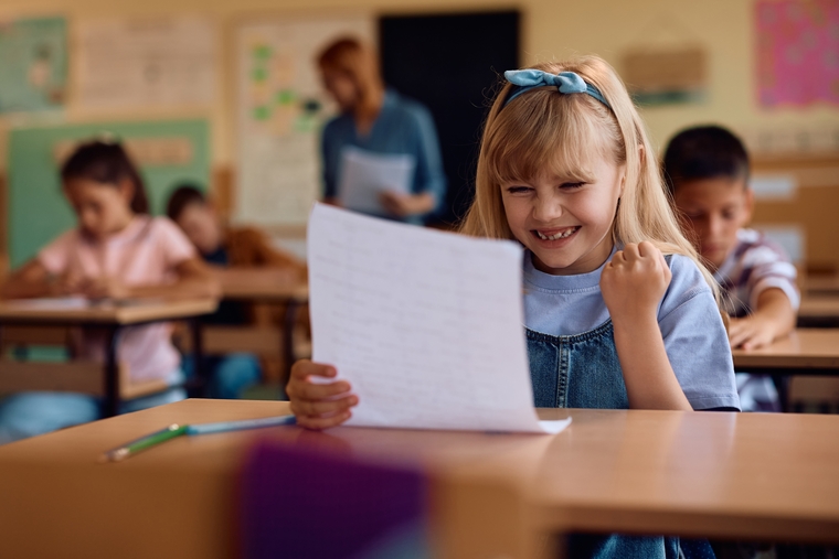 A smiling little girl holds a piece of paper, radiating joy and excitement in her expression.