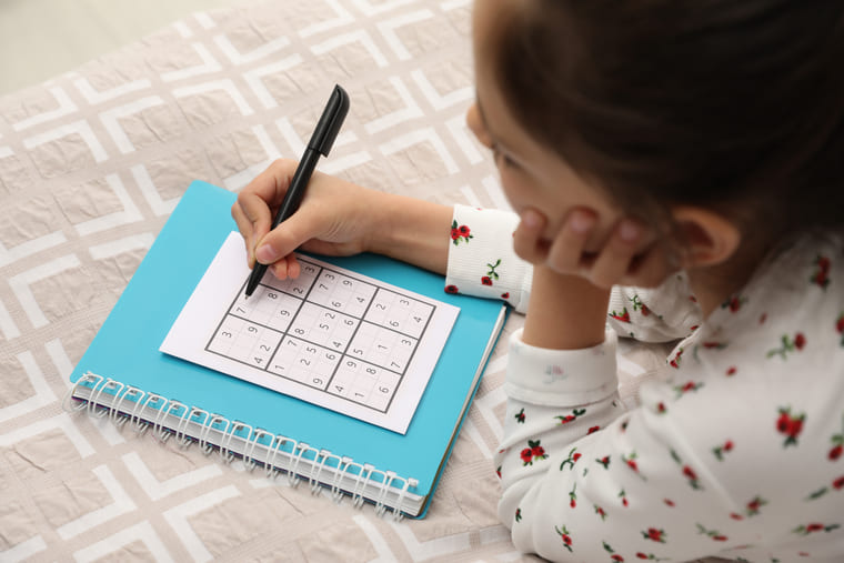 A girl writes in a notebook with a pen, focused on her task.