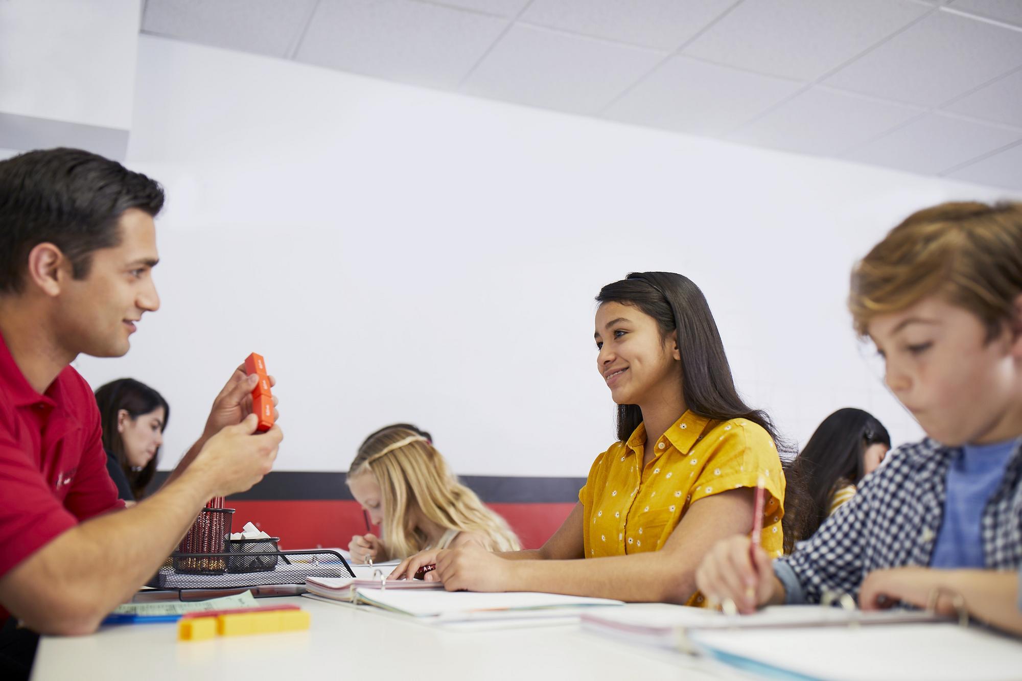 A man sits at a table with children, engaged in a classroom activity together.
