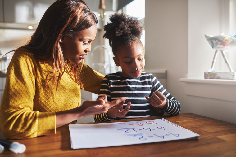 A woman and a child sit at a table, focused on a piece of paper between them.