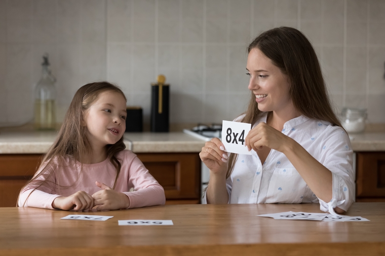 A woman and a young girl joyfully playing with a deck of cards on a table, smiling and engaged in the game.