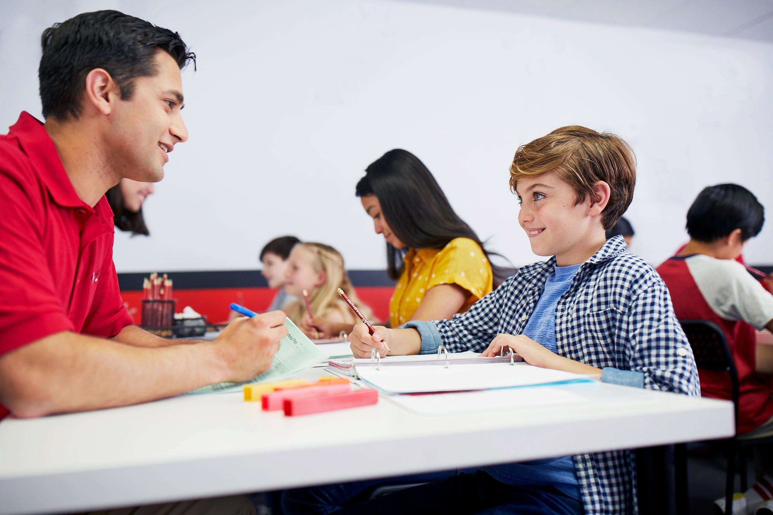 A man and a boy collaborate at a table, with a red pen in front of them, indicating a shared project or discussion.