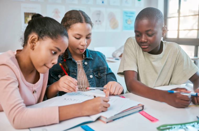 Three children focused on their homework at desks in a bright classroom, surrounded by educational materials.