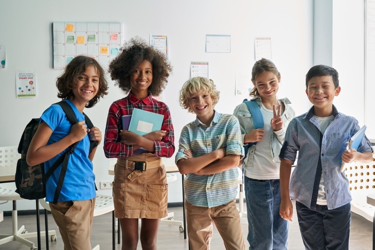 A group of children stands in a classroom, each holding books and engaged in a learning activity.