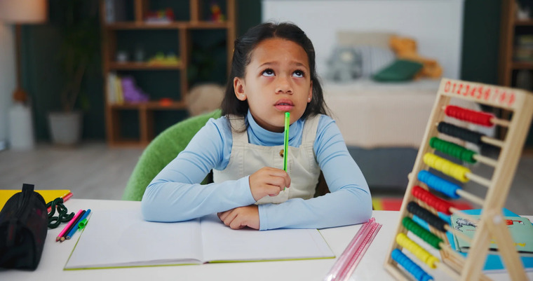A young girl sits at a desk, focused on her work with a pencil in hand and a calculator beside her.