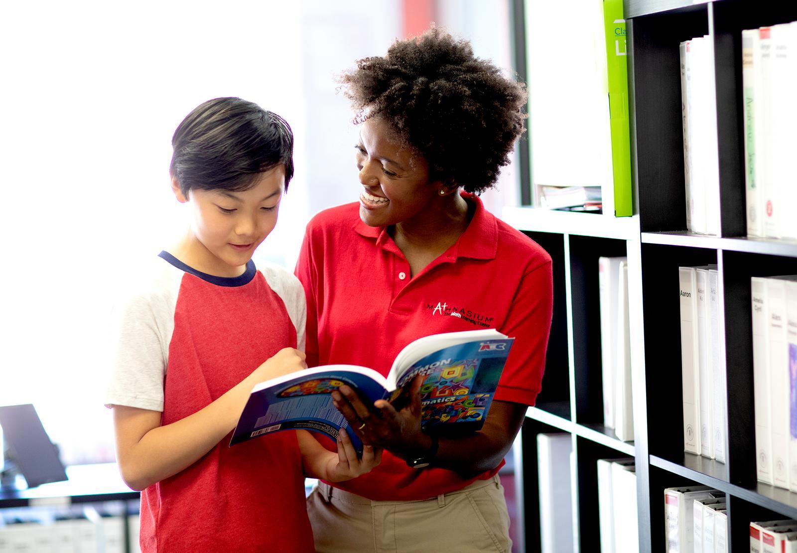 A tutor and her student, a boy, are focused on a book during a learning session.