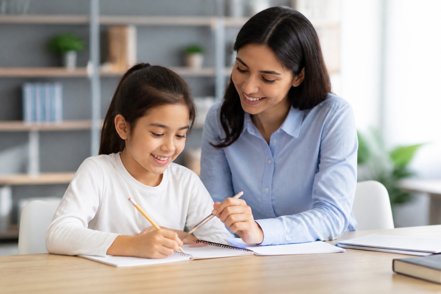 Child and tutor working together on math problems at a table, smiling