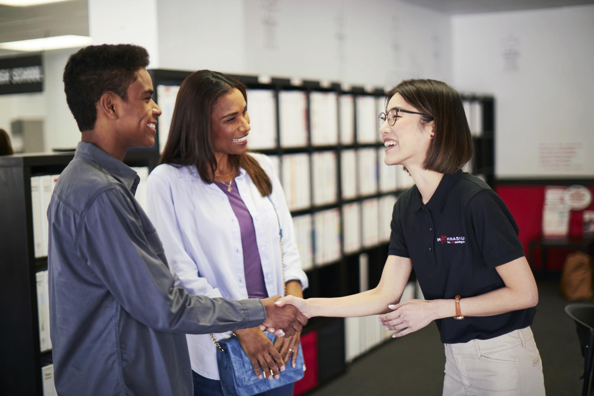 A handshake occurs between a tutor and a family member in an office setting, representing collaboration in learning.