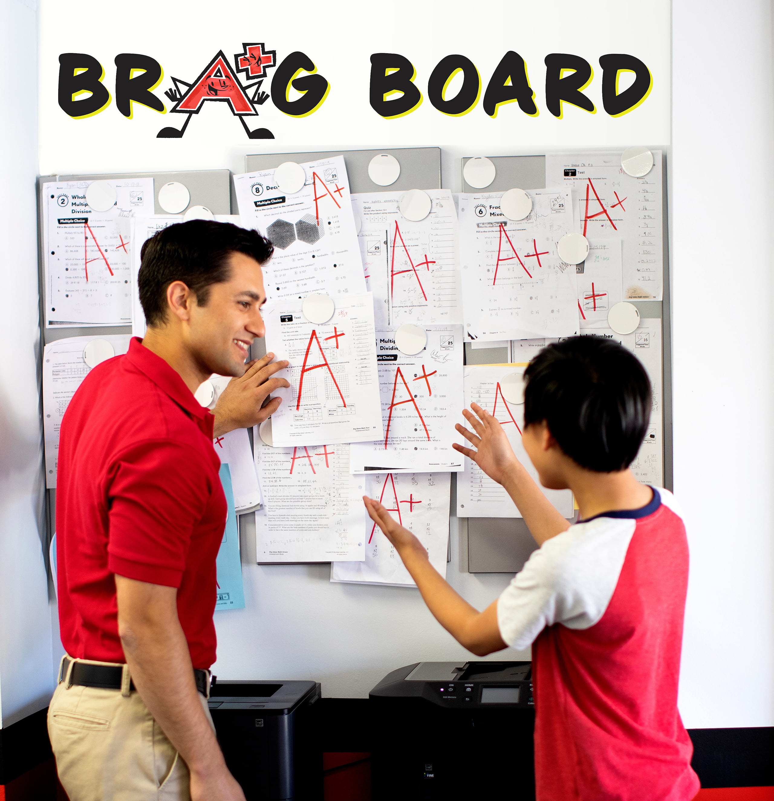 A tutor and a student standing next to a board will well-done math tests.