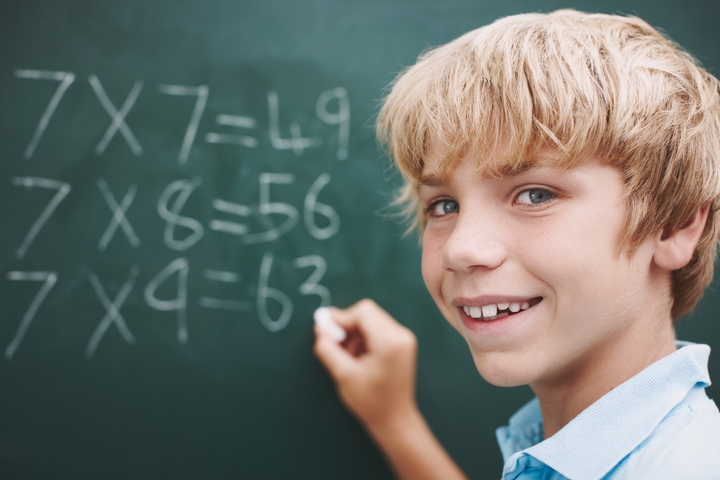 Child next to a chalkboard studying math.