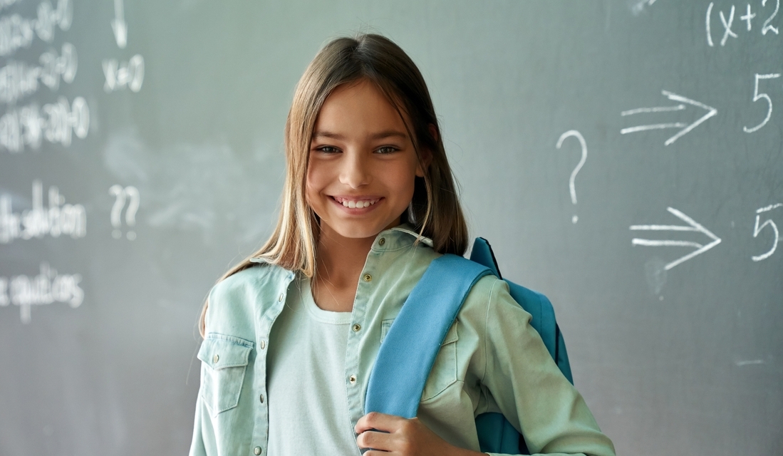 Confident student standing in front of a chalkboard with math problems, smiling with a backpack on