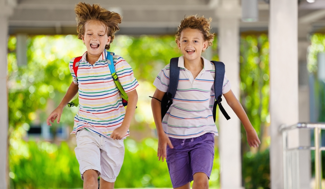 Two happy children with backpacks running outdoors on the last day of school