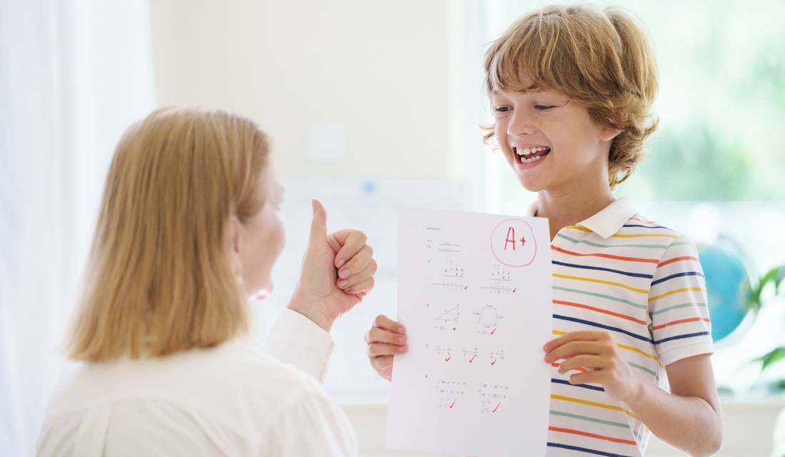Smiling student proudly shows an A+ math test to a parent