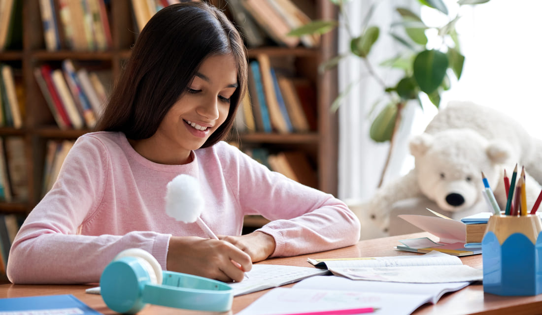 Happy smiling school girl pupil studying math at home sitting at desk.
