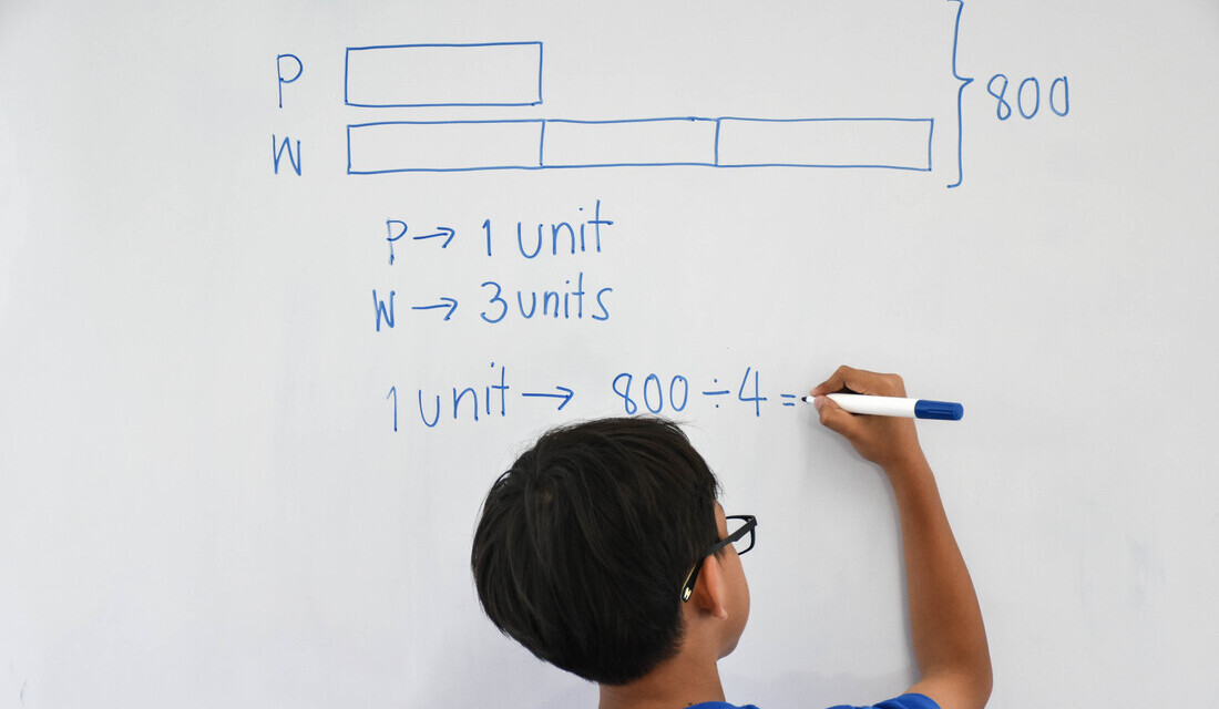 Student solving a bar model math problem on a whiteboard