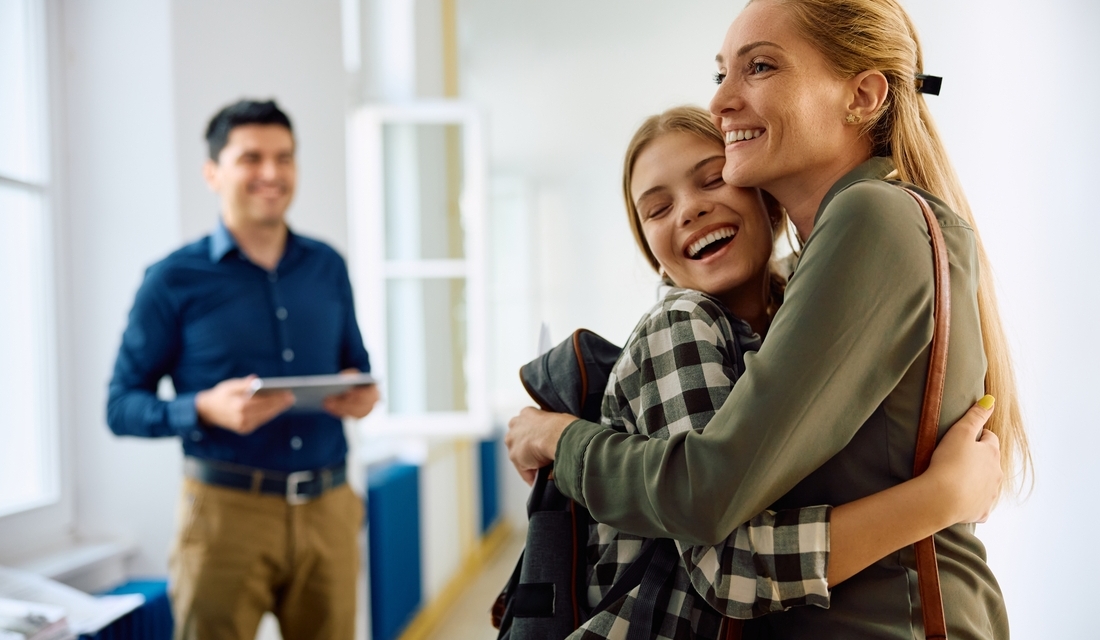 Happy mother and daughter embracing after successful meeting with math teacher in school.